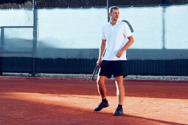 Il giovane gioca a tennis all'aperto sul campo da tennis al mattino