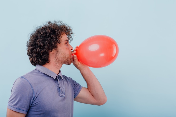 Foto il giovane gonfia un pallone rosso.