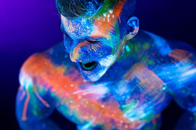 Il giovane grida Vernice fluorescente sul viso e torso muscoloso in studio girato con luce UV