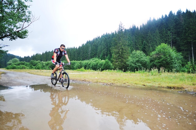 il giovane guida la mountain bike sul fiume d'acqua