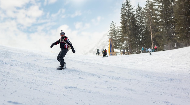 Il giovane guida lo snowboard e si gode una soleggiata giornata invernale sui pendii delle montagne.