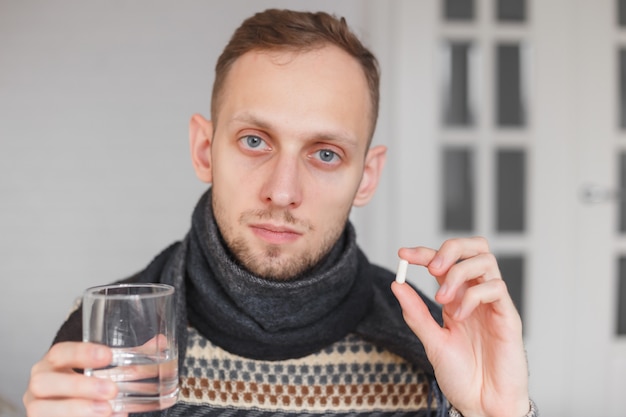 Il giovane ha l'influenza. Tenendo la capsula antibiotica e un bicchiere d'acqua