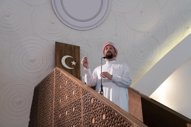Il giovane imam arabo musulmano tiene un discorso sulla preghiera del venerdì pomeriggio nella moschea. I musulmani si sono riuniti per la preghiera del venerdì pomeriggio nella moschea e stanno ascoltando il discorso dell'imam