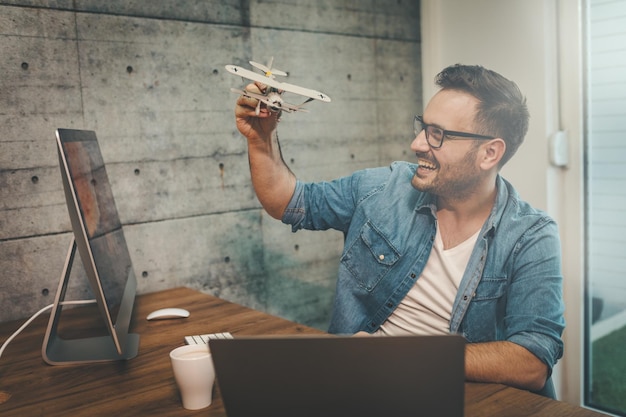 Il giovane imprenditore freelance allegro di successo si diverte e mostra un modellino di aeroplano, spiegando come vola.