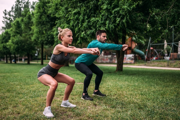 Il giovane in buona salute e la donna che fanno lo squat si esercita all&#39;aperto.