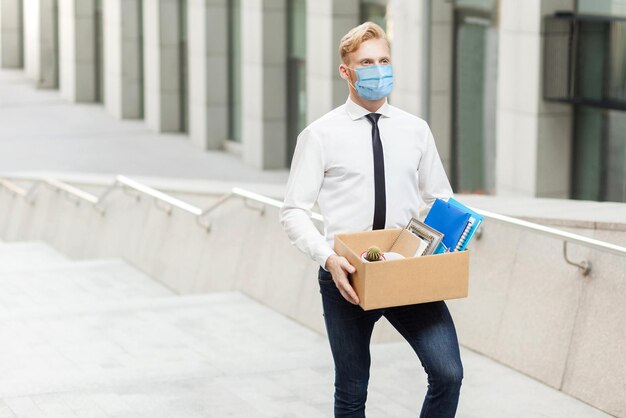 Il giovane in camicia bianca con maschera medica chirurgica ha un nuovo lavoro che va a un nuovo lavoro migliore