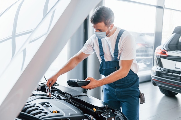 Il giovane in camicia bianca e uniforme blu ripara l'automobile