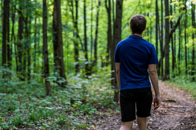 Il giovane in maglietta blu cammina e guarda intorno alla foresta di autunno