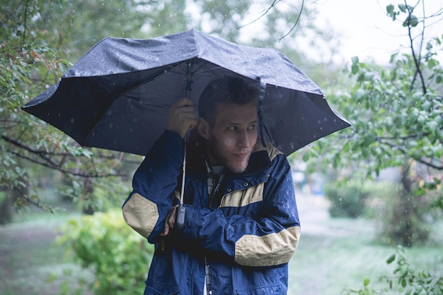 Il giovane in piedi sotto l'ombrello protegge dalle forti piogge tropicali nelle foreste
