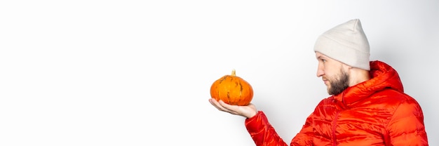 Il giovane in una giacca rossa, il cappello tiene una zucca e la guarda