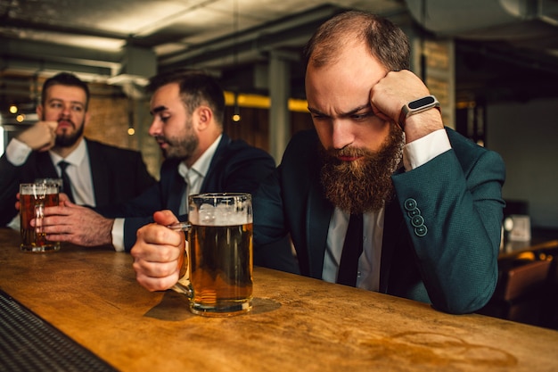 Il giovane in vestito si siede e dorme. Solleva la testa. Guy hold boccale di birra. Altri due impiegati siedono dietro e parlano.