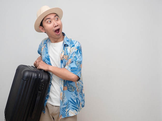 Il giovane indossa la camicia da spiaggia con cappello e si sente stupito dal bagaglio da stiva delle vacanze
