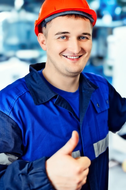 Il giovane ingegnere con il casco mostra i pollici in su I pollici in su Ottimo umore e buoni affari Il lavoratore positivo in abiti da lavoro sorride e guarda nella fotocamera