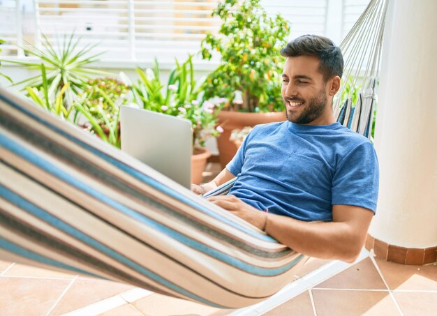 Il giovane ispanico si è rilassato lavorando utilizzando il computer portatile sdraiato sull'amaca in terrazza.