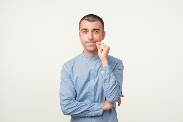 Il giovane latino in camicia blu tiene l'indice sulle labbra cerca di mantenere la cospirazione Cerca di mantenere i segreti