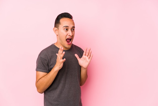 Il giovane latino in posa in un muro rosa urla forte, tiene gli occhi aperti e le mani tese.