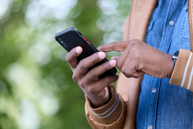 Il giovane libero professionista nero lavora online utilizzando uno smartphone ovunque