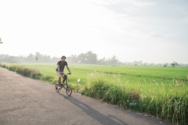 Il giovane maschio indossa i caschi per guidare bici pieghevoli nelle risaie