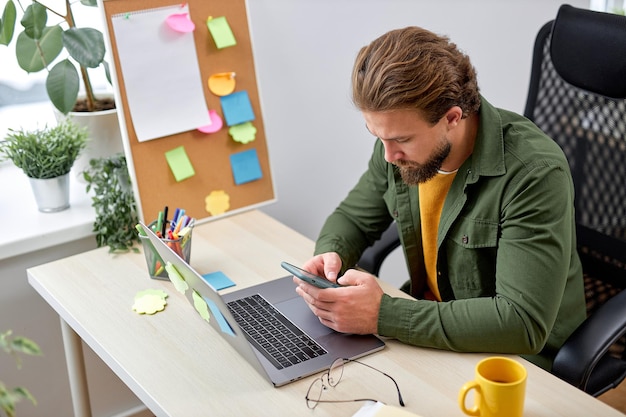 Il giovane maschio si siede usando lo smartphone, riposandosi durante il lavoro in un ufficio moderno e luminoso, da solo. ragazzo caucasico barbuto in abbigliamento casual prendi una pausa digitando il messaggio. uomini d'affari, lavoro, successo