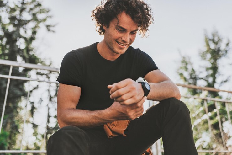 Il giovane maschio sorridente felice indossa la maglietta nera e indossa l'orologio per strada Uomo allegro che posa per la pubblicità con lo spazio della copia all'aperto nella strada della città Concetto della gente