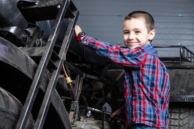 Il giovane meccanico di auto del ragazzino sogna allegramente di essere veloce in sella a una moto nel garage di una stazione di servizio. Un bambino che sorride e che sta vicino su un vecchio ATV
