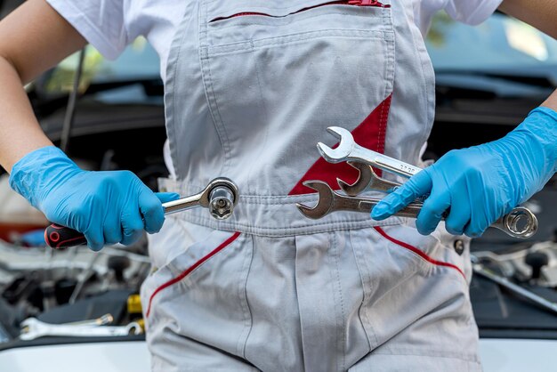 Il giovane meccanico professionista femminile ispeziona sotto il cofano di un'auto in un'officina di riparazioni auto