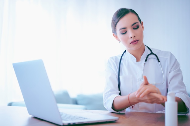 Il giovane medico femminile applica il gel antisettico prima di iniziare la giornata lavorativa. Lavoratore ospedaliero che pulisce le mani utilizzando disinfettante alcolico liquido