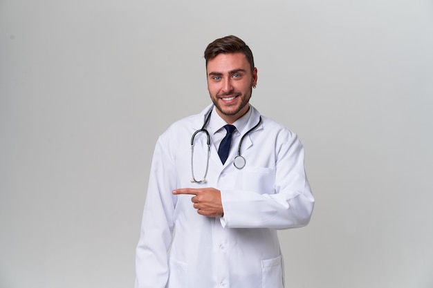 Il giovane medico moderno bello in un abito medico bianco sta nello studio su un bianco. Studente in tirocinio presso un'università di medicina.