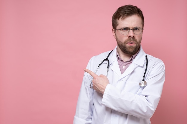 Il giovane medico serio con uno stetoscopio intorno al collo punta il dito di lato e guarda con ansia