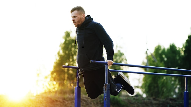 Il giovane muscoloso bello ha un allenamento di allenamento al parco al tramonto