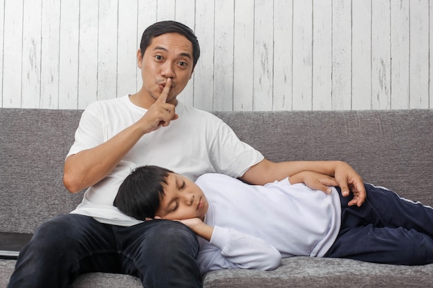 Il giovane padre asiatico in maglietta bianca sta mostrando il dito indice alla bocca come segno di essere tranquillo quando è così