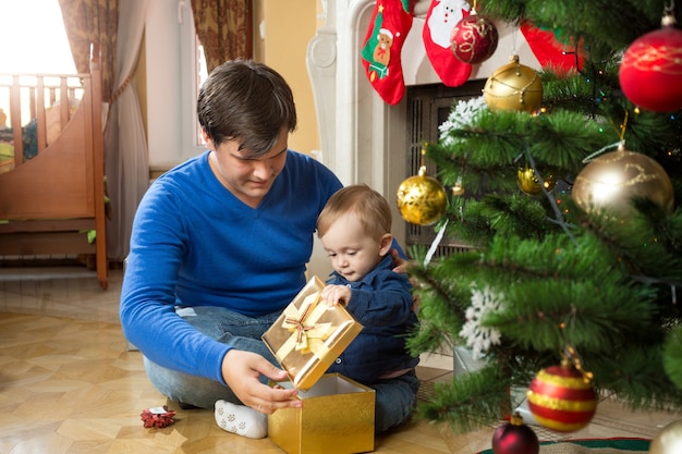 Il giovane padre e il bambino carino aprono i regali di Natale sul pavimento