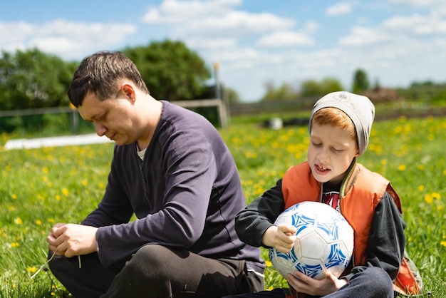 Il giovane padre e il figlio si siedono sull'erba in estate dopo aver giocato insieme a calcio per divertirsi insieme