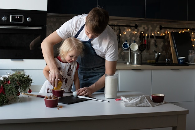 Il giovane padre e la sua piccola figlia graziosa fanno felicemente insieme i lecca-lecca di Natale. La cucina è decorata per il nuovo anno. Attività di svago invernale familiare tradizionale