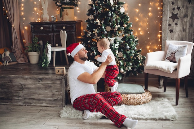 Il giovane papà bello tiene un bambino vicino all'albero di natale