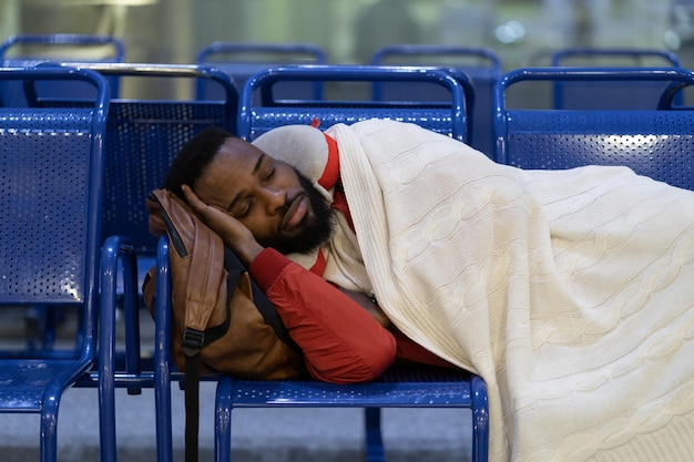 Il giovane passeggero africano che dorme sotto il plaid in attesa del volo sente la connessione lunga notte fredda