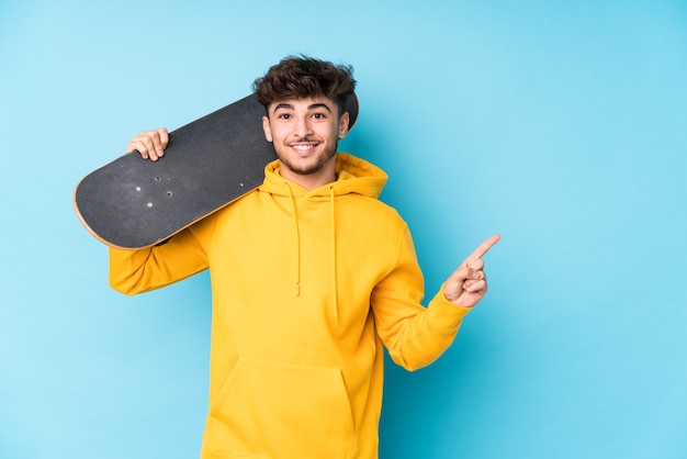 Il giovane pattinatore arabo uomo isolato sorridendo e indicando da parte, mostrando qualcosa in uno spazio vuoto.