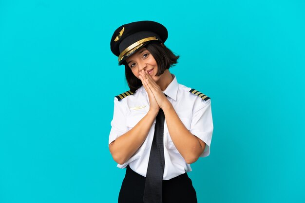 Il giovane pilota dell'aeroplano sopra fondo blu isolato tiene insieme il palmo. La persona chiede qualcosa