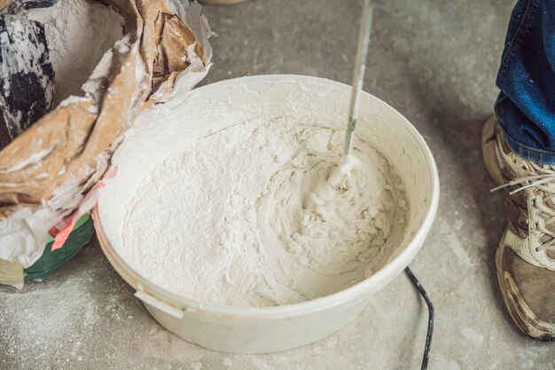 Il giovane pittore maschio impasta lo stucco con l'acqua in un secchio usando un miscelatore portatile per creare miscele