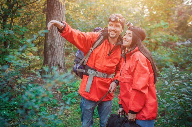 Il giovane positivo sta vicino alla donna e indica in avanti. Lei si appoggia a lui. Sorridono insieme. Le persone sono nella foresta verde.