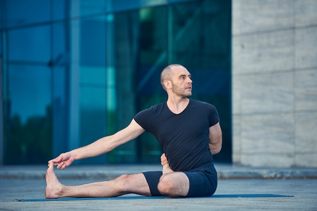 Il giovane pratica yoga all'aperto sullo sfondo di una città moderna