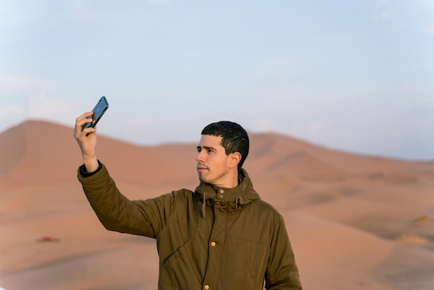 Il giovane prende un selfie con il suo smartphone nel mezzo del deserto