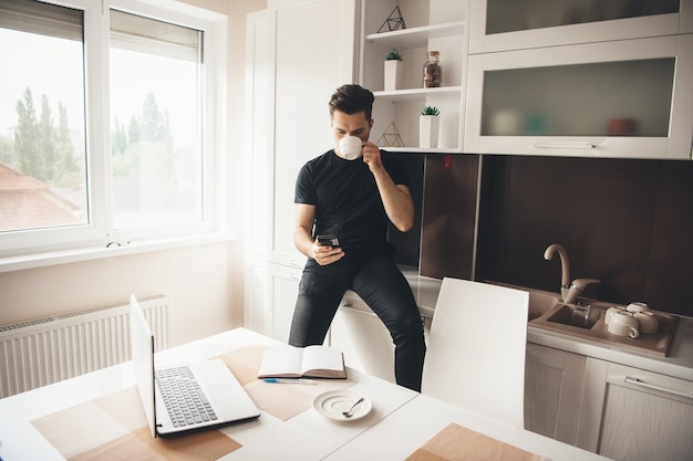 Il giovane programmatore caucasico sta avendo una pausa bevendo un caffè e chiacchierando al telefono in cucina