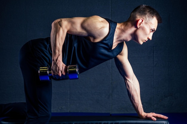 Il giovane rafforza i muscoli delle mani dei manubri in palestra