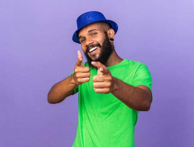 Il giovane ragazzo afroamericano sorridente che indossa un cappello da festa punta alla telecamera