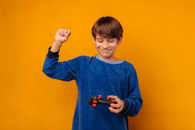 Il giovane ragazzo allegro sta tenendo un joystick e un braccio per essere un vincitore