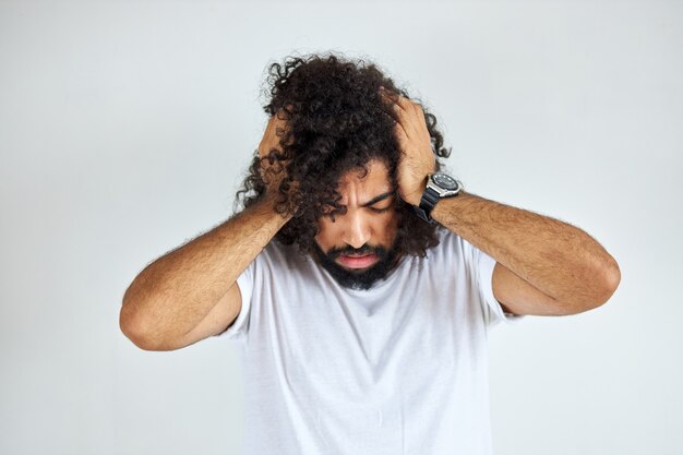 Il giovane ragazzo arabo indiano con i capelli lunghi ha mal di testa, soffre di emicrania