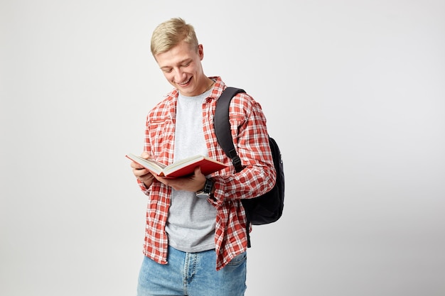 il giovane ragazzo biondo legge un libro sullo sfondo bianco in studio