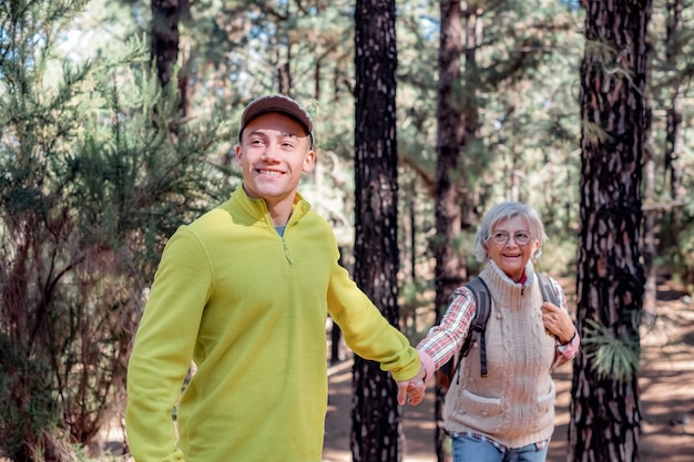 Il giovane ragazzo caucasico aiuta sua nonna a fare un'escursione nella foresta di montagna Famiglia multigenerazionale sorridente