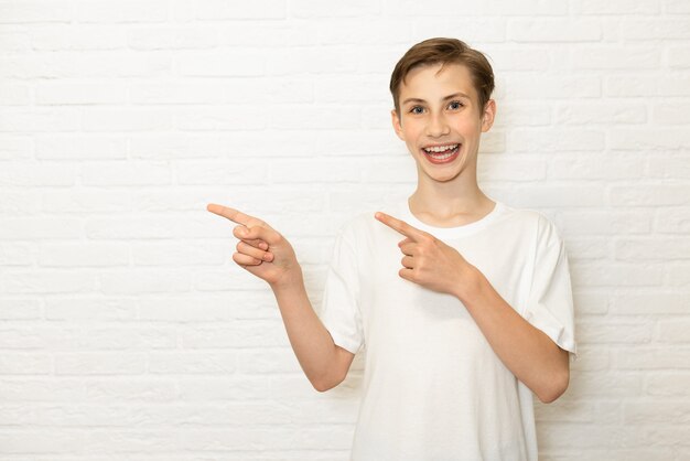 Il giovane ragazzo teenager sorridente mostra il suo dito a lato